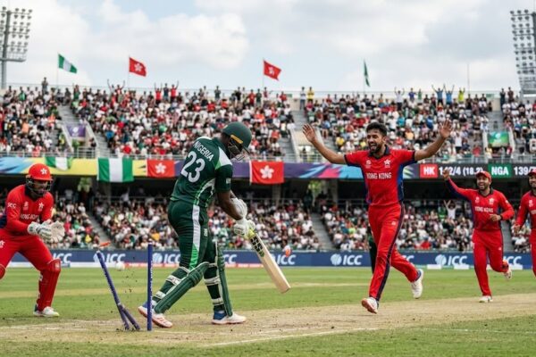 Hong Kong and Nigeria players preparing for an ICC T20 World Cup Qualifier match at Tolerance Oval in Abu Dhabi under floodlights with fans in the background.